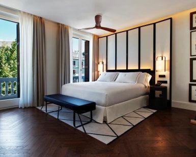 El Gran Hotel Montesol: Curio Collection by Hilton en Ibiza cuenta con una elegante habitación con una cama grande, ventanas de suelo a techo, ventilador de techo y arte enmarcado, que encarna a la perfección la esencia vibrante de Ibiza. - ForTwo - Planes para parejas