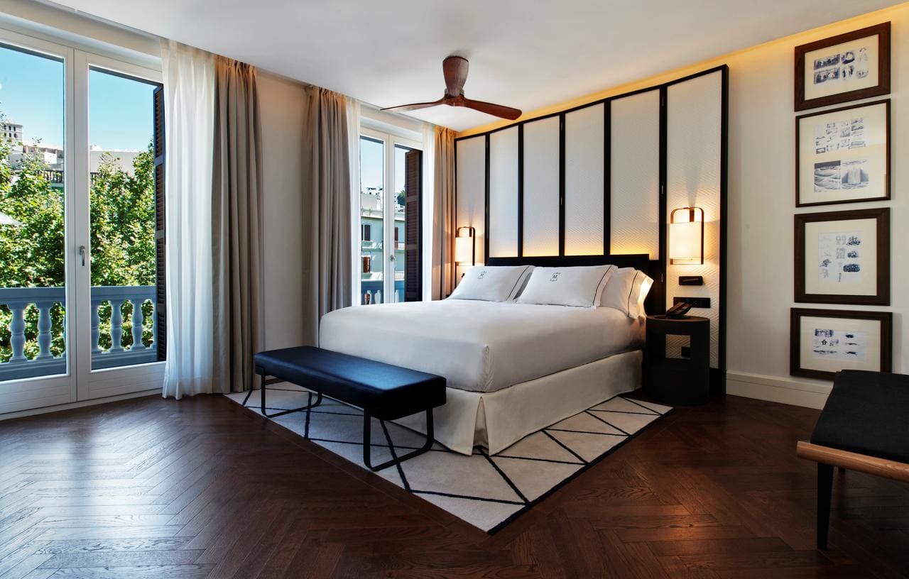 El Gran Hotel Montesol: Curio Collection by Hilton en Ibiza cuenta con una elegante habitación con una cama grande, ventanas de suelo a techo, ventilador de techo y arte enmarcado, que encarna a la perfección la esencia vibrante de Ibiza. - ForTwo - Planes para parejas