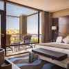 Descubra la elegancia en la Gran Suite Mediterránea con terraza en el hotel Miramar (Barcelona), una moderna habitación con una gran cama, almohadas decorativas y una terraza con vistas a frondosos árboles y aguas serenas. - ForTwo - Planes para parejas