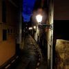 Un callejón estrecho al anochecer, iluminado por farolas que proyectan un brillo misterioso sobre los edificios, crea el escenario perfecto para el Tour nocturno por la Granada Paranormal contra un cielo azul oscuro. - ForTwo - Planes para parejas