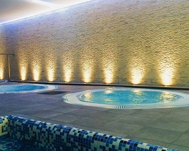 El spa interior del Granada Palace ofrece el "Circuito en Spa + masaje" con bañeras de hidromasaje redondas, suelo de baldosas y una pared de piedra con iluminación cálida para la relajación. - ForTwo - Planes para parejas