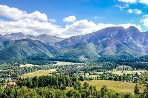 La "Visita guiada a Zakopane y a las Tatras (Cracovia)" muestra un paisaje montañoso con exuberante vegetación, un pintoresco pueblo y un cielo azul salpicado de nubes. - ForTwo - Planes para parejas