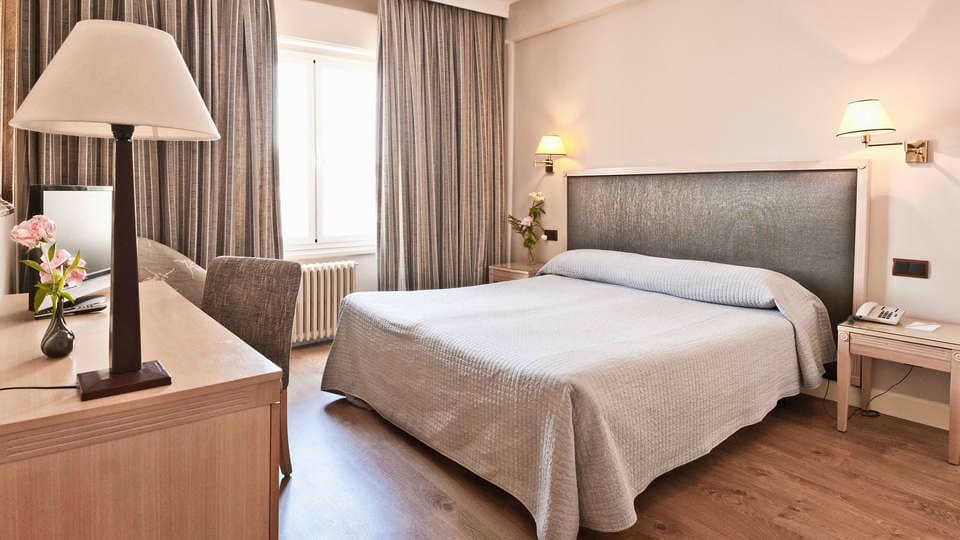 Relájese en una acogedora habitación del Hotel Príncipe Pío con cama doble, escritorio y lámpara. Los tonos neutros y el suelo de madera aportan tranquilidad. Después de explorar la ciudad, disfrute de una "Escapada al Hotel Príncipe Pío con botella de cava y cena en un restaurante a elegir (Madrid)" para completar la velada. - ForTwo - Planes para parejas