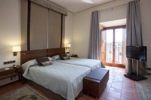 El Parador de Cáceres ofrece un acogedor alojamiento con dos camas individuales, mesitas de noche, TV de pared y un gran ventanal con cortinas que se abre a un encantador balcón. - ForTwo - Planes para parejas