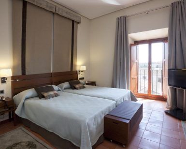 El Parador de Cáceres ofrece un acogedor alojamiento con dos camas individuales, mesitas de noche, TV de pared y un gran ventanal con cortinas que se abre a un encantador balcón. - ForTwo - Planes para parejas