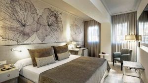 Disfrute de la escapada perfecta en una habitación moderna del Hotel Escapada Sallés Pere IV de Barcelona, con una cama grande, arte floral, un cómodo sillón, lámpara y ventanas con cortinas transparentes que dejan entrar la luz natural. El paquete incluye desayuno, acceso al spa y bebida de bienvenida. - ForTwo - Planes para parejas