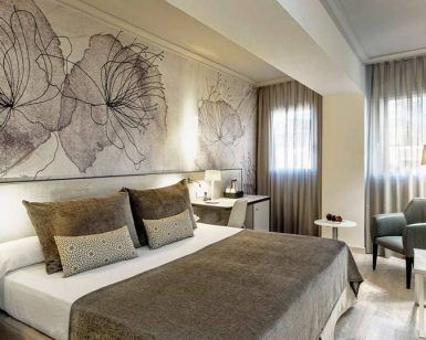 Disfrute de la escapada perfecta en una habitación moderna del Hotel Escapada Sallés Pere IV de Barcelona, con una cama grande, arte floral, un cómodo sillón, lámpara y ventanas con cortinas transparentes que dejan entrar la luz natural. El paquete incluye desayuno, acceso al spa y bebida de bienvenida. - ForTwo - Planes para parejas