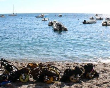 En la tranquila playa de Buceo Calahonda, el equipo del "Curso de buceo en Granada" descansa listo para explorar el mar tranquilo. Las embarcaciones se mecen suavemente cerca de un acantilado escarpado, capturando la encantadora belleza costera de Granada. - ForTwo - Planes para parejas