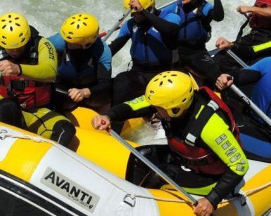 Un grupo de aventureros ataviados con cascos y trajes de neopreno se adentran en las agitadas aguas en una embarcación neumática amarilla, disfrutando de un emocionante "Rafting de iniciación en Granada - Tramo alto del río Guadalfeo". - ForTwo - Planes para parejas