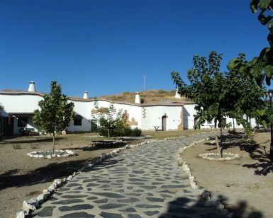 Un camino de piedra conduce a encantadoras casas blancas con chimeneas en Guadix, enclavadas como joyas bajo un cielo azul nítido, capturando la esencia de "Una noche en cueva romántica de turismo rural (Guadix)", donde los árboles escasos se alzan como centinelas. - ForTwo - Planes para parejas