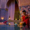 Un hombre vierte suavemente agua sobre la cabeza de una mujer mientras ella flota pacíficamente en una lujosa y ornamentada piscina cubierta, evocando la relajante experiencia del Baño con masaje MIMMA 15 en Hammam Al Ándalus Málaga. - ForTwo - Planes para parejas