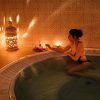 Una mujer en bikini se relaja en un jacuzzi, rodeada de velas y faroles ornamentados, creando la encantadora atmósfera de un Baño árabe en pareja con masaje sencillo en Medina Aljarafe (Sevilla). - ForTwo - Planes para parejas
