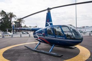 Un elegante helicóptero azul en el helipuerto, enmarcado por palmeras y un barco distante, inspira sueños de un emocionante "Vuelo en helicóptero sobre el Cañón Tajo de los Vados", que ofrece impresionantes vistas. - ForTwo - Planes para parejas