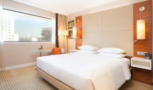 Alójese en el Hotel Hilton de Barcelona y disfrute de una experiencia moderna con una cama grande, elegantes mesitas de noche y una mesa redonda con una planta. Disfrute de las vibrantes vistas de la ciudad desde su ventana, capturando la esencia de este icónico destino. - ForTwo - Planes para parejas