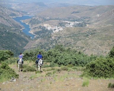 Dos personas disfrutan de una Ruta a caballo de 2 horas por Sierra Nevada en Güéjar Sierra, montando a caballo por laderas cubiertas de hierba con vistas panorámicas a las impresionantes montañas y ríos de Sierra Nevada. - ForTwo - Planes para parejas
