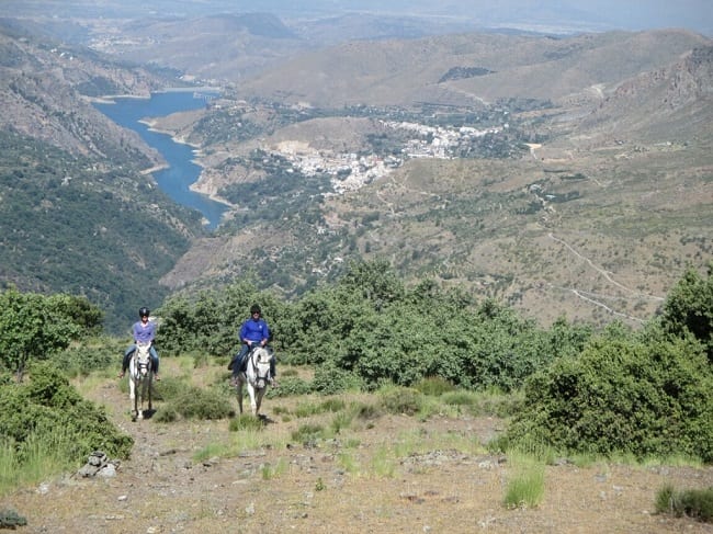 Dos personas disfrutan de una Ruta a caballo de 2 horas por Sierra Nevada en Güéjar Sierra, montando a caballo por laderas cubiertas de hierba con vistas panorámicas a las impresionantes montañas y ríos de Sierra Nevada. - ForTwo - Planes para parejas