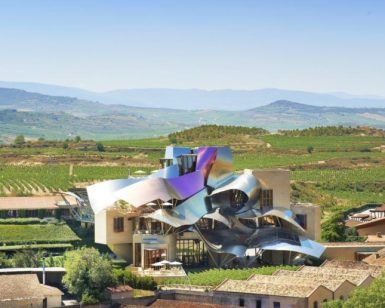 Bajo un cielo azul claro, la estructura metálica y ondulada de la Bodega Marqués de Riscal en Álava se alza entre viñedos, invitándote a una inolvidable Visita a la bodega Marqués de Riscal (Álava). - ForTwo - Planes para parejas