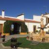 El patio del Hotel El Moral exhibe una encantadora fuente de piedra, rodeada de mesas, botellas de vino y un edificio blanco y fresco bajo el cielo azul, ideal para la "Escapada romántica al hotel El Moral con visita a sus bodegas y cata de vinos (Badajoz). - ForTwo - Planes para parejas