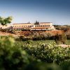 El paisaje de viñedos en el corazón de Cuenca revela una vista lejana del Complejo Enoturístico Finca La Estacada bajo un cielo azul claro, proporcionando una experiencia enoturística inigualable. - ForTwo - Planes para parejas