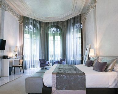 Descubra una estancia refinada en Hospes Palacio de los Patos con una elegante habitación con una cama grande, decoración moderna, TV, escritorio y zona de estar junto a ventanales. Eleva tu experiencia con "Disfruta de un fin de semana de lujo con spa en Hospes Palacio de los Patos (Granada). - ForTwo - Planes para parejas