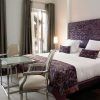 El elegante dormitorio, con cama doble, detalles en morado y un ambiente de spa, ofrece un "Fin de semana de lujo con spa en el Hotel Hospes Puerta Alcalá (Madrid)". Dos sillas y una mesa de cristal realzan los amplios ventanales con cortinas, ideales para relajarse. - ForTwo - Planes para parejas