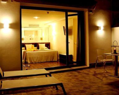 Relájese en una acogedora habitación de hotel con cama doble, con vistas a un patio con tumbonas y una mesa pequeña. Disfrute de la cálida iluminación mientras saborea un cóctel después de disfrutar de la Escapada con piscina, cóctel y visita guiada (Sevilla). - ForTwo - Planes para parejas