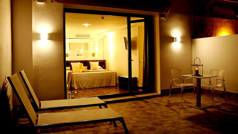 Relájese en una acogedora habitación de hotel con cama doble, con vistas a un patio con tumbonas y una mesa pequeña. Disfrute de la cálida iluminación mientras saborea un cóctel después de disfrutar de la Escapada con piscina, cóctel y visita guiada (Sevilla). - ForTwo - Planes para parejas