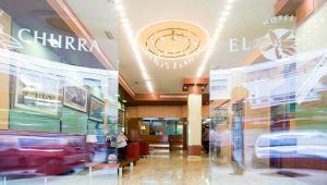 El vestíbulo del hotel, con una hermosa lámpara de araña y cómodos asientos, ofrece un entorno ideal para la "Escapada romántica con desayuno en el centro de Murcia", con la animada confusión de personas y coches en el exterior capturando la vibrante energía del centro de Murcia. - ForTwo - Planes para parejas