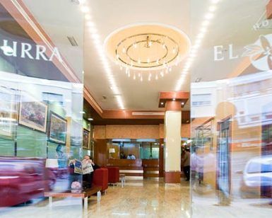 El vestíbulo del hotel, con una hermosa lámpara de araña y cómodos asientos, ofrece un entorno ideal para la "Escapada romántica con desayuno en el centro de Murcia", con la animada confusión de personas y coches en el exterior capturando la vibrante energía del centro de Murcia. - ForTwo - Planes para parejas
