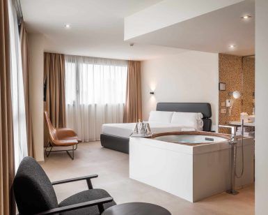 Disfrute de la comodidad moderna en el Hotel con jacuzzi SB Diagonal Zero en Barcelona, que cuenta con una lujosa cama doble, un cómodo sillón, un jacuzzi placentero y una amplia ventana con elegantes cortinas beige. - ForTwo - Planes para parejas