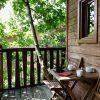 La Habitación Casa del árbol Maitenea del Hotel Jakue (Navarra) incluye un patio de madera con mesa, sillas, tazas y un cuaderno rodeado de frondosos árboles verdes que crean un ambiente tranquilo. - ForTwo - Planes para parejas