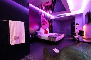 Situado en Torrejón de Ardoz, el Hotel de adultos para hacer cosas de adultos ofrece una moderna habitación con una vibrante iluminación violeta, un mural artístico de rostros, una acogedora cama, una elegante zona de estar y una lujosa toalla sobre la mampara de cristal para los adultos que buscan tranquilidad. - ForTwo - Planes para parejas