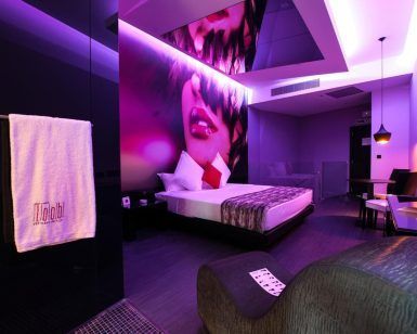 Situado en Torrejón de Ardoz, el Hotel de adultos para hacer cosas de adultos ofrece una moderna habitación con una vibrante iluminación violeta, un mural artístico de rostros, una acogedora cama, una elegante zona de estar y una lujosa toalla sobre la mampara de cristal para los adultos que buscan tranquilidad. - ForTwo - Planes para parejas