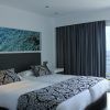Disfrute de la comodidad del Hotel Náutico Ebeso en Ibiza con una habitación que ofrece dos camas, ropa de cama estampada elegante, un balcón con vista al mar y una impresionante obra de arte de agua azul sobre el cabecero. - ForTwo - Planes para parejas