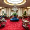 El lujoso lobby del Hotel Wellington Madrid exhibe una alfombra roja, elegantes asientos y lámparas de araña bajo un gran tragaluz adornado con plantas vibrantes. - ForTwo - Planes para parejas