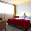 Disfrute de una Noche Deluxe con desayuno y cava en SB Diagonal Zero. Relájese en nuestra moderna habitación, con una cama grande con manta roja, sillón, mesitas de noche y elegantes ventanas con cortinas beige, creando el ambiente perfecto para relajarse. - ForTwo - Planes para parejas