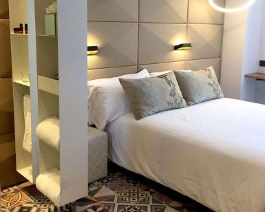 Experimente una moderna habitación de hotel con estanterías abiertas, una elegante cama, suelo estampado, apliques de pared y vistas increíbles del encanto de Barcelona con Escapada en hotel 4 estrellas. - ForTwo - Planes para parejas