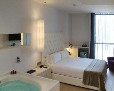 Disfrute de un remanso de paz en el Hotel con jacuzzi SB Plaza Europa (Barcelona), donde la acogedora habitación incluye una cama lujosa, iluminación relajante y cortinas transparentes que enmarcan la ventana. Relájese con estilo en su jacuzzi privado. - ForTwo - Planes para parejas