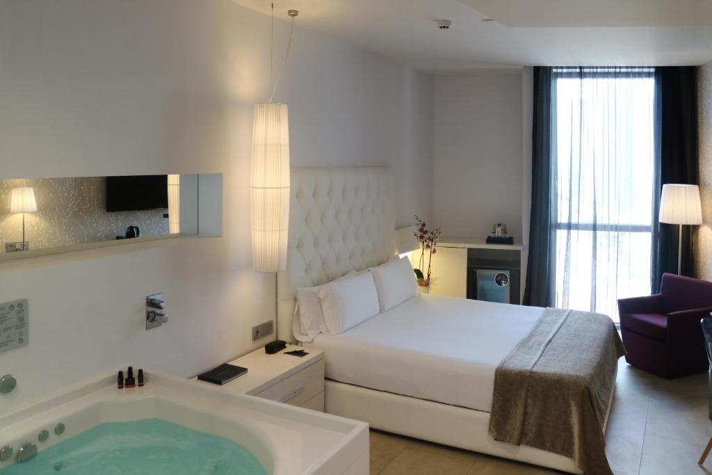 Disfrute de un remanso de paz en el Hotel con jacuzzi SB Plaza Europa (Barcelona), donde la acogedora habitación incluye una cama lujosa, iluminación relajante y cortinas transparentes que enmarcan la ventana. Relájese con estilo en su jacuzzi privado. - ForTwo - Planes para parejas