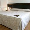 Una cama cuidadosamente hecha con ropa de cama con diseño en espiral, dos mesas de noche con lámparas encendidas y un piso de madera pulida crean un ambiente sereno que recuerda a la experiencia de Escapada en el Hotel Sinagoga con desayuno, bombones y spa (Hervás). - ForTwo - Planes para parejas