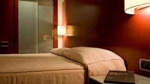 Relájese en una cama doble en el Escapada Hotel Zenit de Valencia, con paredes de madera y una cálida lámpara de pared. Disfrute del casco histórico, saboree una paella y acceda a la sauna y al gimnasio. - ForTwo - Planes para parejas