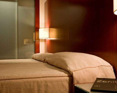 Relájese en una cama doble en el Escapada Hotel Zenit de Valencia, con paredes de madera y una cálida lámpara de pared. Disfrute del casco histórico, saboree una paella y acceda a la sauna y al gimnasio. - ForTwo - Planes para parejas
