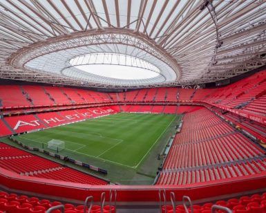 El majestuoso Estadio San Mamés de Bilbao se encuentra vacío con sus asientos rojos contrastando con el exuberante campo verde bajo un gran techo ovalado retráctil, esperando ansiosamente la vitalidad del próximo Tour por el estadio San Mamés (Bilbao). - ForTwo - Planes para parejas