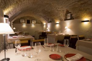 El Menú Aljibe del Restaurante Alacena de las Monjas (Granada) ofrece una acogedora experiencia gastronómica con mesas elegantemente dispuestas y platos de autor rojos bajo un techo de ladrillo arqueado, evocando el encanto de un aljibe escondido en Granada. - ForTwo - Planes para parejas