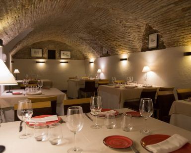 El Menú Aljibe del Restaurante Alacena de las Monjas (Granada) ofrece una acogedora experiencia gastronómica con mesas elegantemente dispuestas y platos de autor rojos bajo un techo de ladrillo arqueado, evocando el encanto de un aljibe escondido en Granada. - ForTwo - Planes para parejas