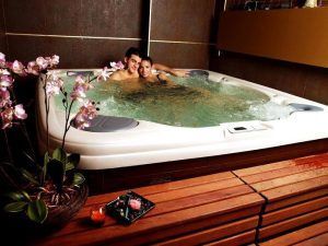 Una pareja relajada en un "Jacuzzi privado con tu pareja + cava + bombones", rodeados de orquídeas, a la luz de las velas en un banco de madera, disfrutando de cava burbujeante y deliciosos bombones. - ForTwo - Planes para parejas