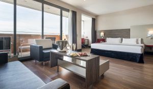 Descubre la elegancia de la Junior Suite: el secreto de Ilunion Hotels (Barcelona), con un diseño moderno que incluye una amplia cama, acogedora zona de estar, balcón y una mesa preparada con snacks y champán frío. - ForTwo - Planes para parejas