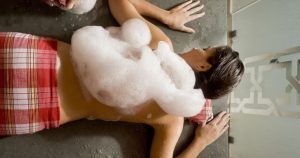 Una persona yace boca abajo en un spa, cubierta de burbujas de jabón sobre una toalla roja y blanca, evocando la tranquila experiencia del "Hammam en Córdoba: baño árabe con kessa y masaje MIDRA 30. - ForTwo - Planes para parejas