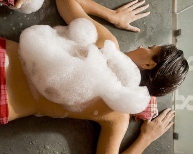 Una persona yace boca abajo en un spa, cubierta de burbujas de jabón sobre una toalla roja y blanca, evocando la tranquila experiencia del "Hammam en Córdoba: baño árabe con kessa y masaje MIDRA 30. - ForTwo - Planes para parejas
