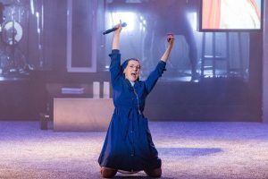 En el Teatro Lara de Madrid, una persona con un vestido azul se arrodilla con los brazos en alto y sostiene un micrófono, lo que recuerda las escenas dinámicas de "La llamada". - ForTwo - Planes para parejas